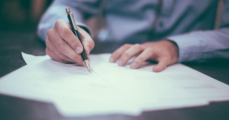 Person signing real estate documents comparing offer letter and purchase agreement, showing the differences between the two real estate documents